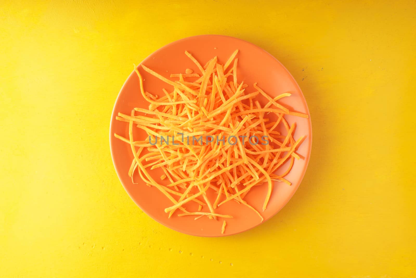 Fresh grated carrot on a yellow background horizontal