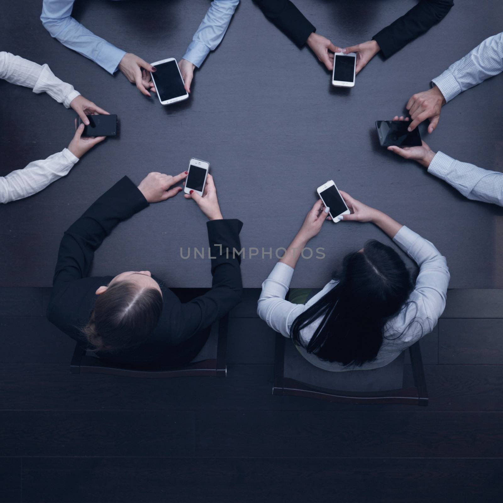 Business people with smartphones sitting around the table, top view