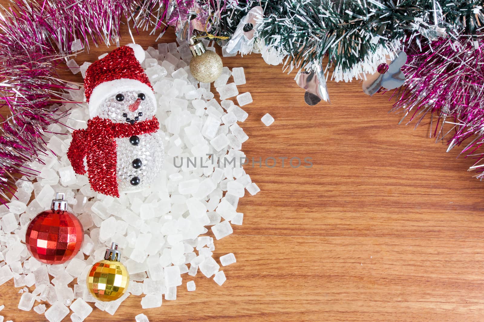 Snow Man on a pile of white crystalline with white background. Red and yellow Christmas Balls Ornaments on wood,