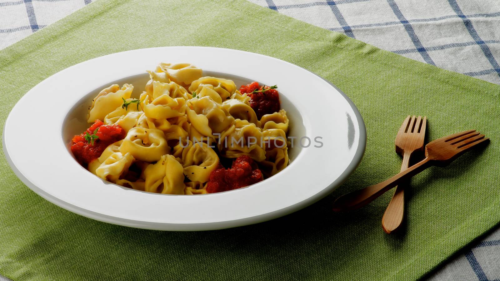 Delicious Meat Cappelletti with Tomato Sauce in White Plate with Wooden Forks closeup on Green Napkin