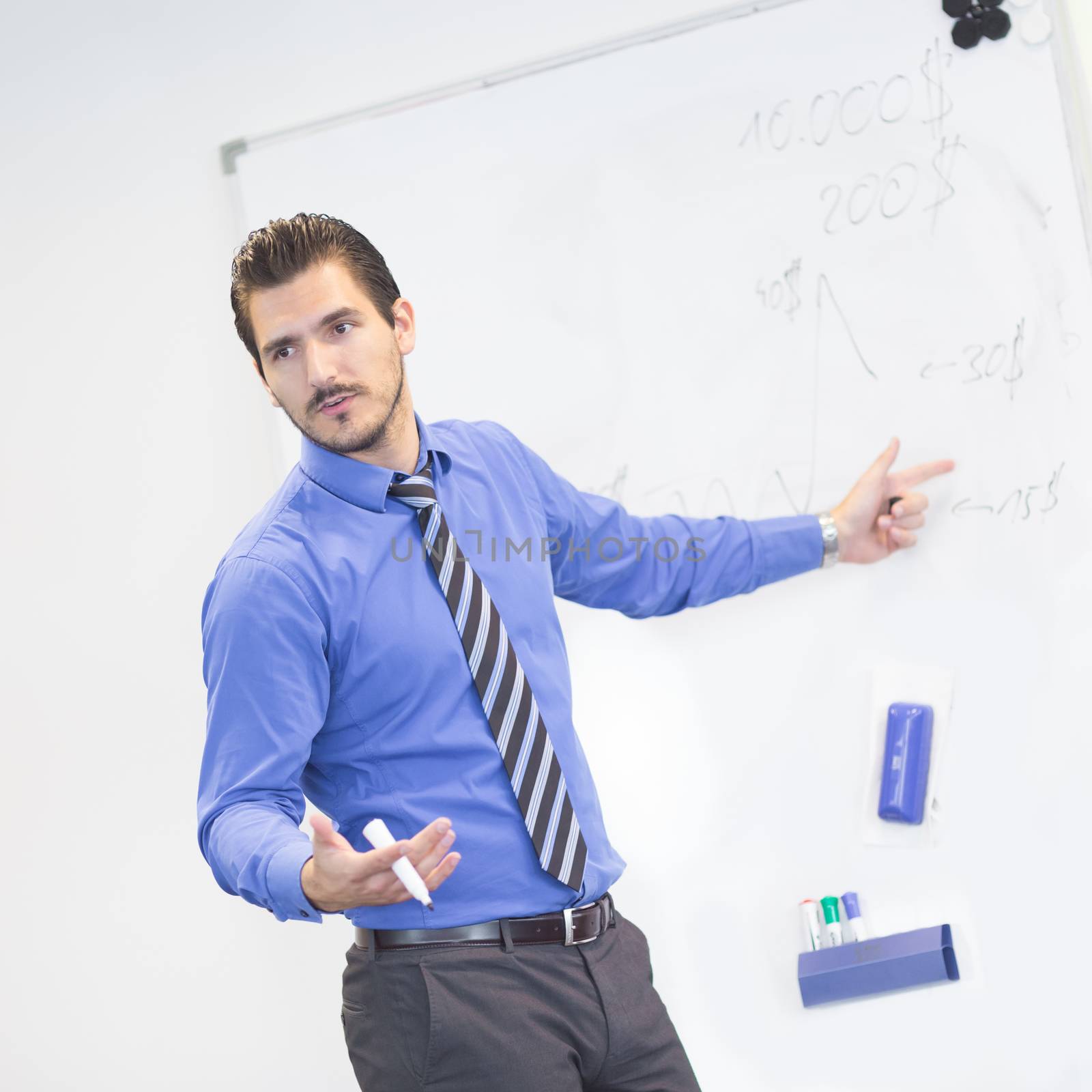 Business man making a presentation in front of whiteboard. Business executive delivering a presentation to his colleagues during meeting or in-house business training, explaining business plans.