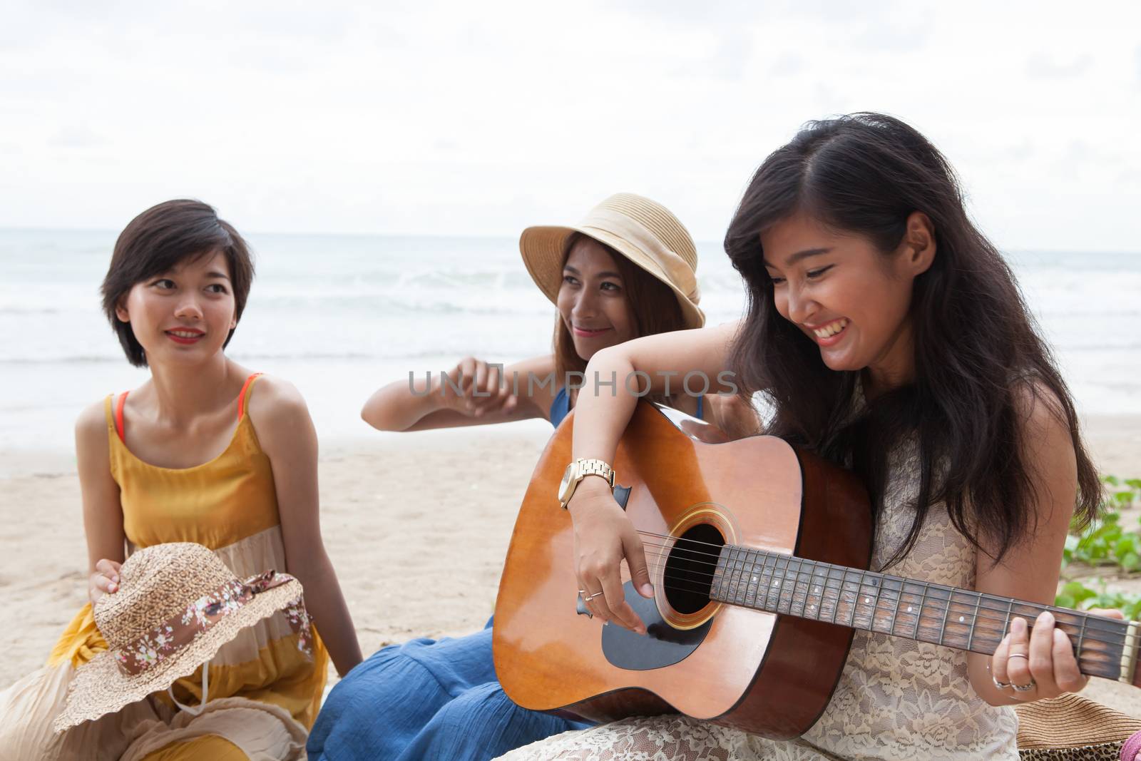 portrait group of young asian woman palying guitar in sea beach picnic party at sea side with happiness face emotion