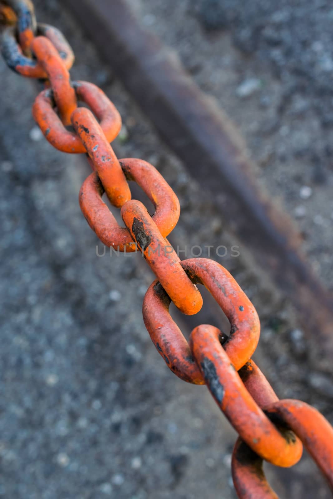 A red colored rusted chain with asphalt in bacground