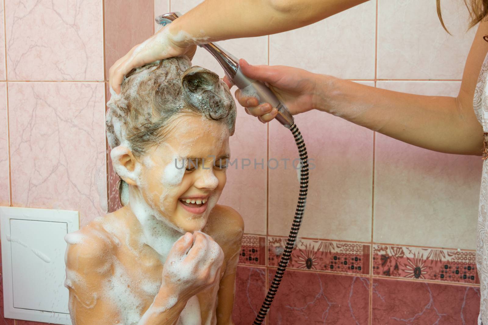 Mom washes the soap and shampoo in the shower with a seven-year daughter