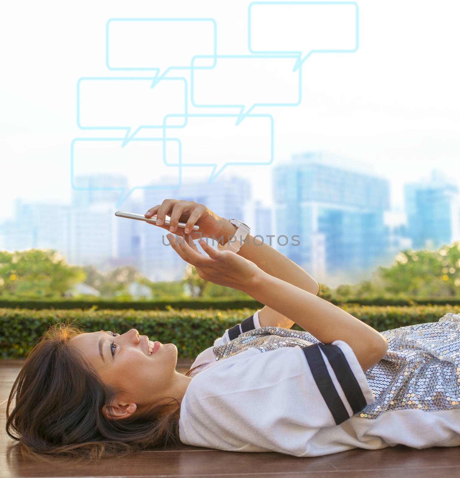 city life style of asian woman lying and touching on mobile phone screen against green environment and urban skylind background