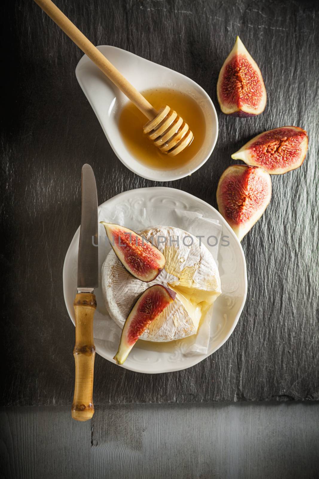 A wheel of melted brie covered in sliced figs and honey  on a stone plate.