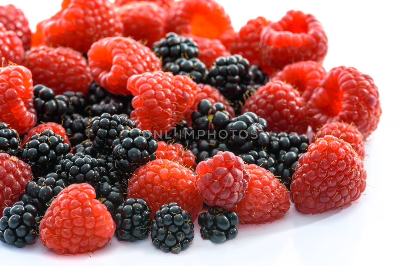 Raspberries and blackberries scattered on a white background