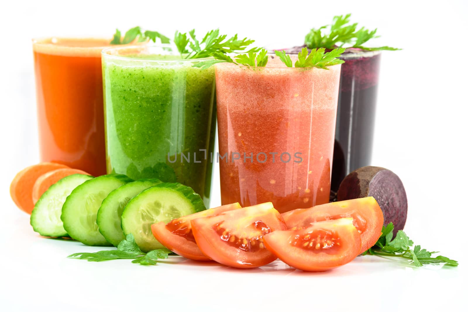 Four vegetable juices in glasses with parsley and vegetables isolated on a white background