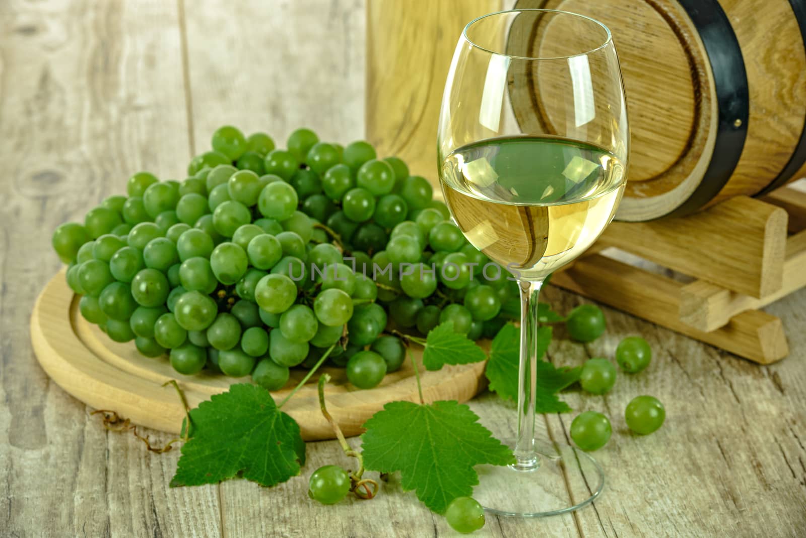 Semi sweet white wine in the cup  next to fresh grapes and a wooden barrel