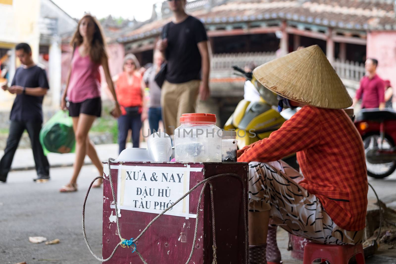 Unidentified old woman in traditional Vietnamese clothes carrying buskets with food on the street in Hoi An city