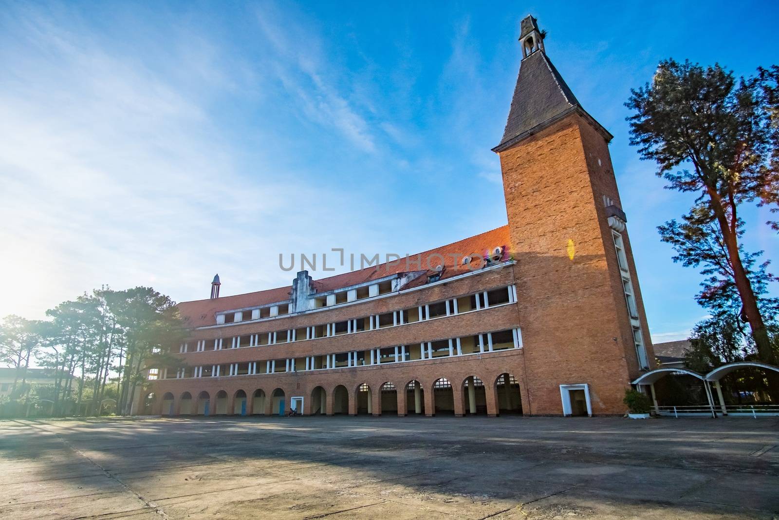 Arched architectural beauty, rustic buildings Pedagogical University in sunny with red roofing tiles impressive pines in Da Lat city, Lam Dong, Vietnam