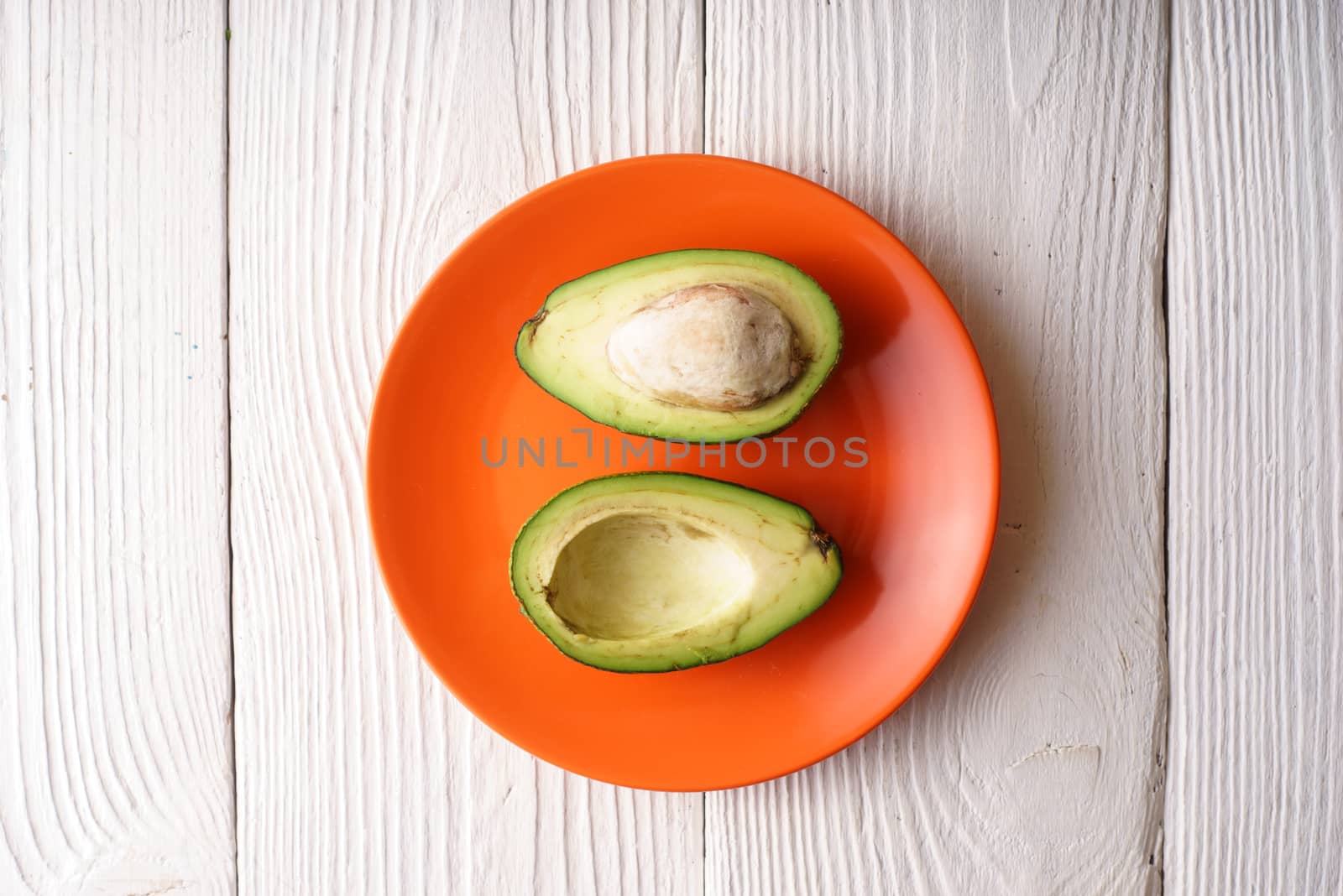 Halves of avocado on the orange plate by Deniskarpenkov