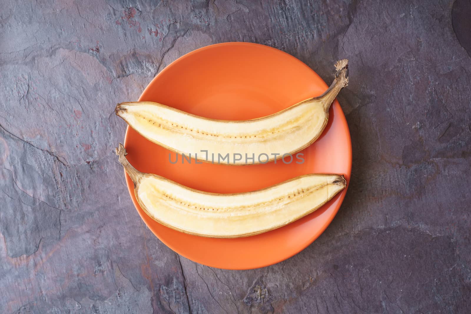 Banana halves lie on orange plate on a slate horizontal