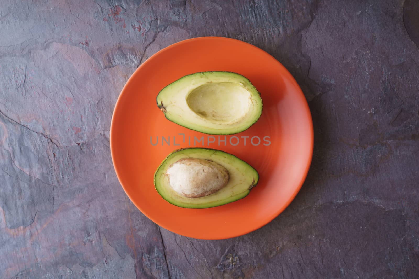 Avocado halves lie on an orange plate on a slate horizontal