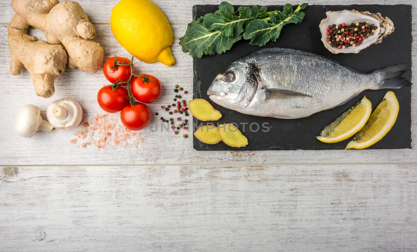 Useful dorado fish, rich in protein, vitamins, Omega 3 with vegetables, lemon and ginger, prepared for cooking on a white wooden table. Top view