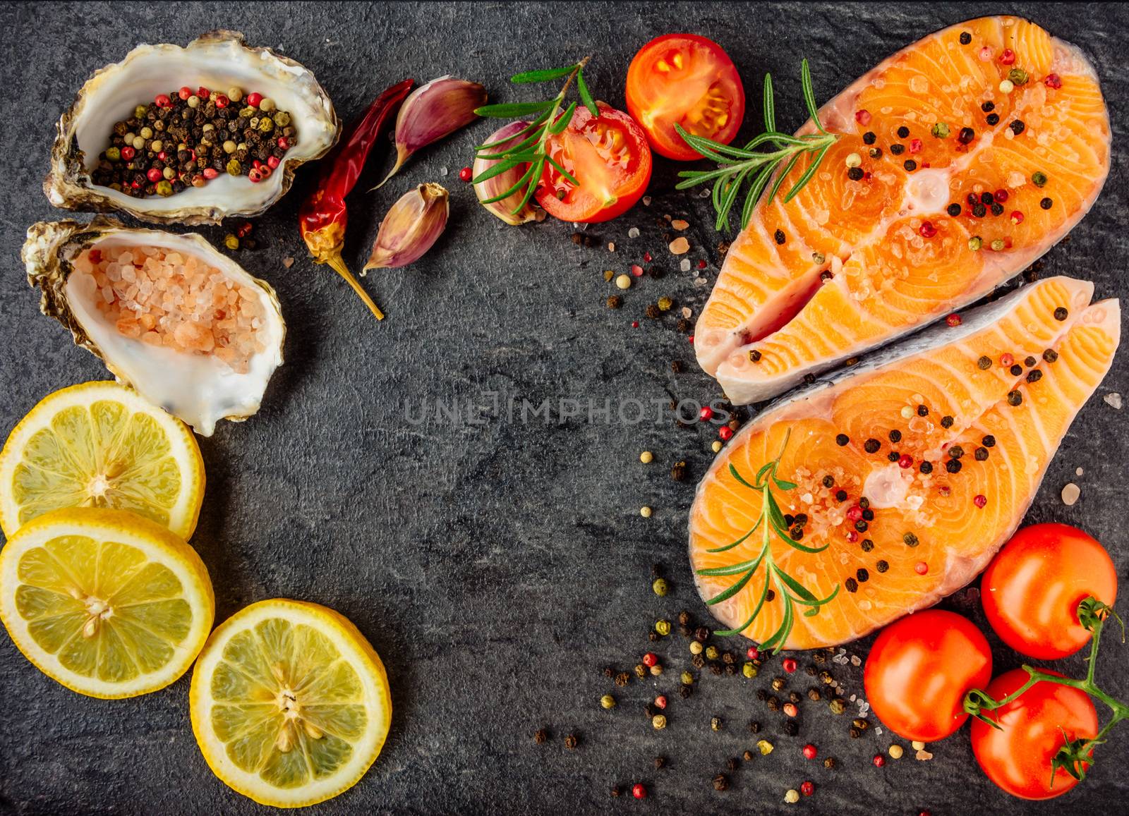 Delicious salmon steak , rich in omega 3 oil, with aromatic herbs and spices with a lemon, tomato, garlic on black background. Healthy and diet food. Top view.