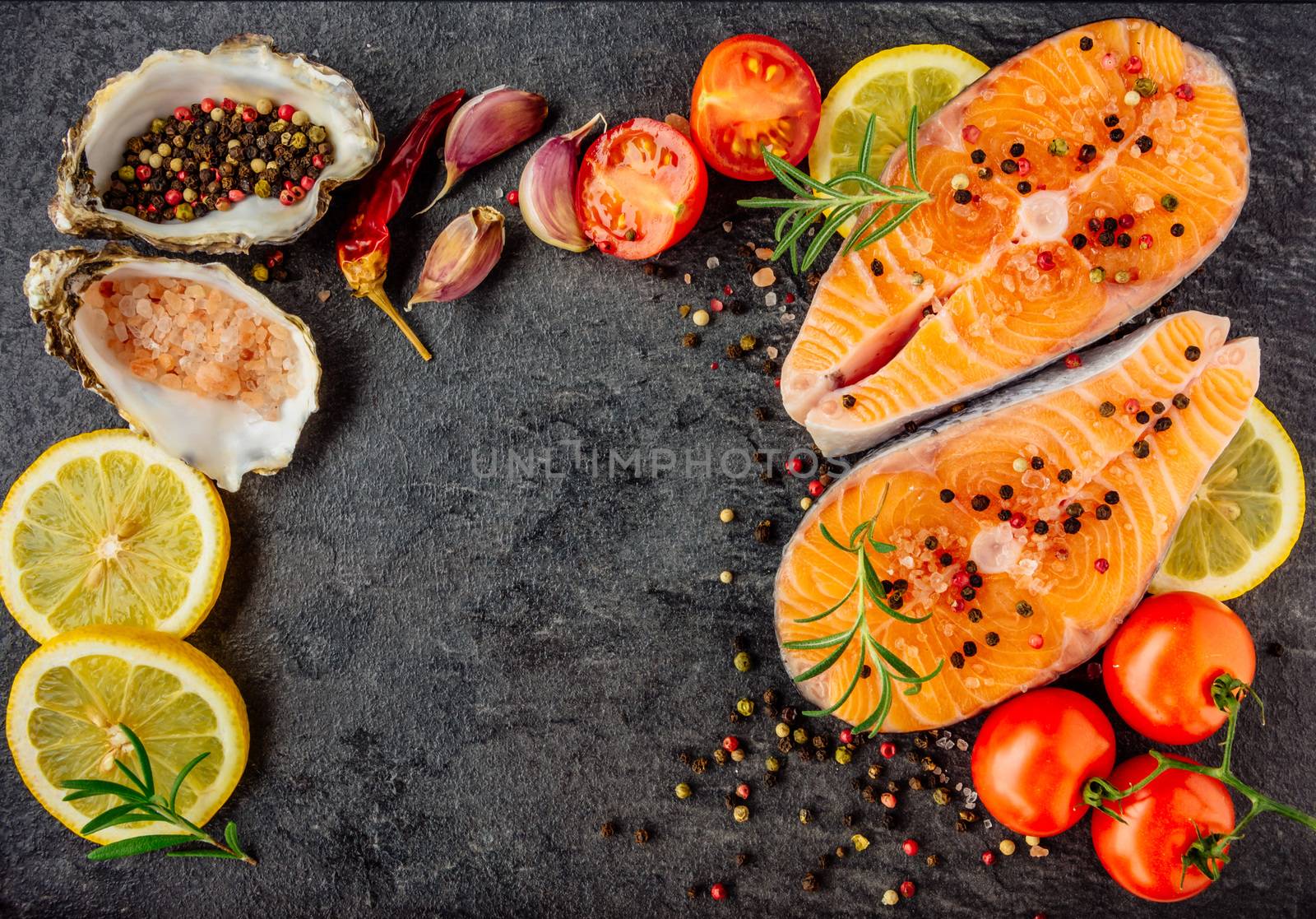 Delicious salmon steak , rich in omega 3 oil, with aromatic herbs and spices with a lemon, tomato, garlic on black background. Healthy and diet food. Top view.