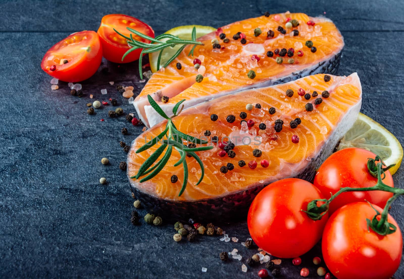Delicious salmon steak , rich in omega 3 oil, with aromatic herbs and spices with a lemon, tomato, garlic on black background. Healthy and diet food.