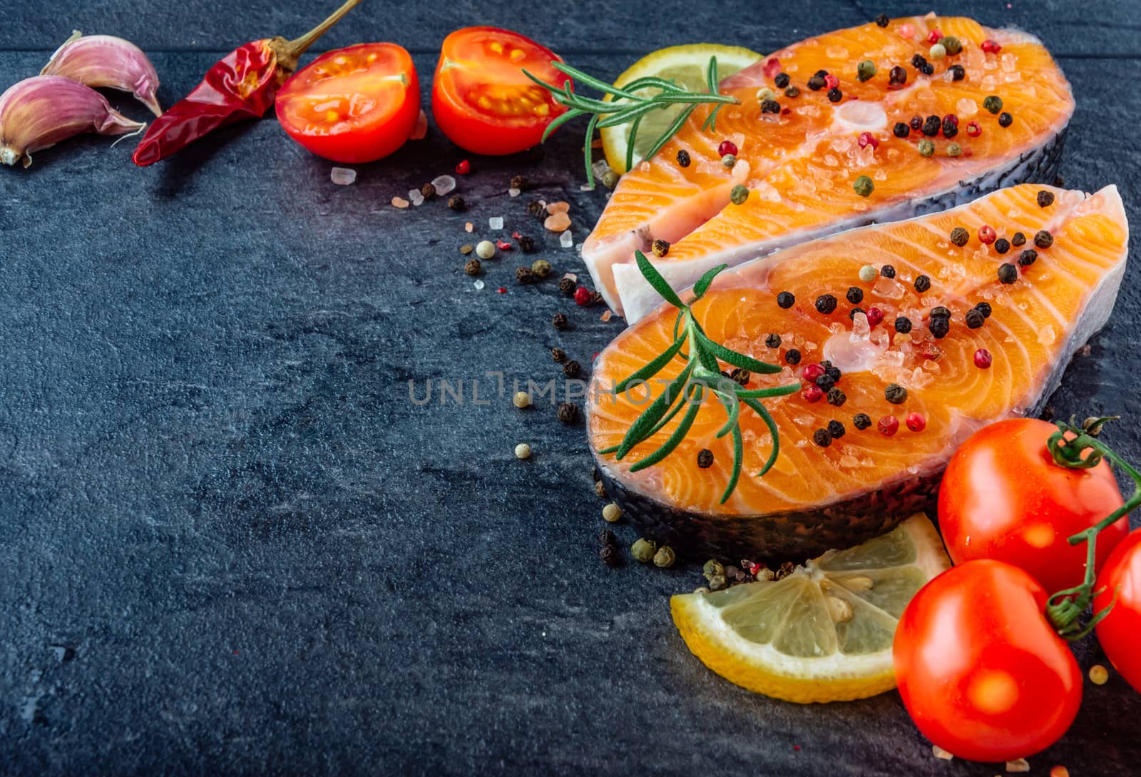Delicious salmon steak , rich in omega 3 oil, with aromatic herbs and spices with a lemon, tomato, garlic on black background. Healthy and diet food.