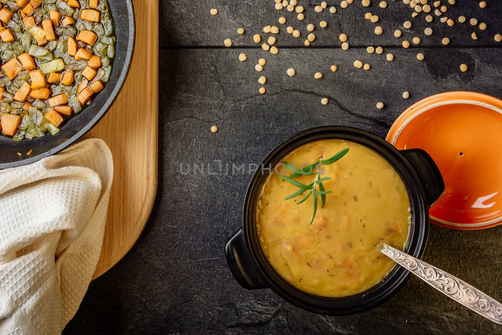 pea soup with carrots and onions in a black pot on a dark table top view