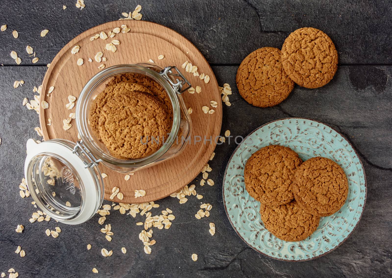 Oat cookies lay on a plate and bank with oatmeal cookies standing on a wooden board top view