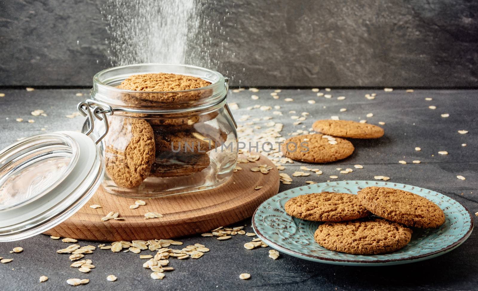 Oat cookies lay on a plate and bank with oatmeal cookies standing on a wooden board.
