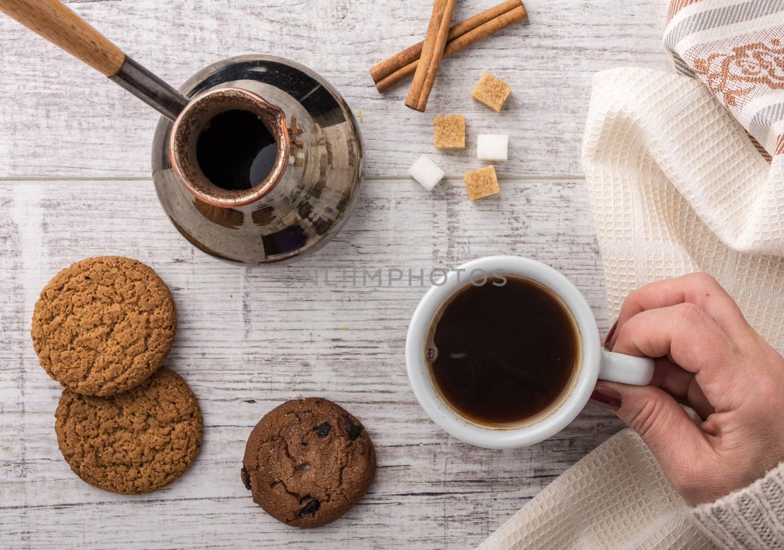 woman drinking coffee with cookies, sugar and honey. coffee maker, cinnamon lying on a white wooden table. 