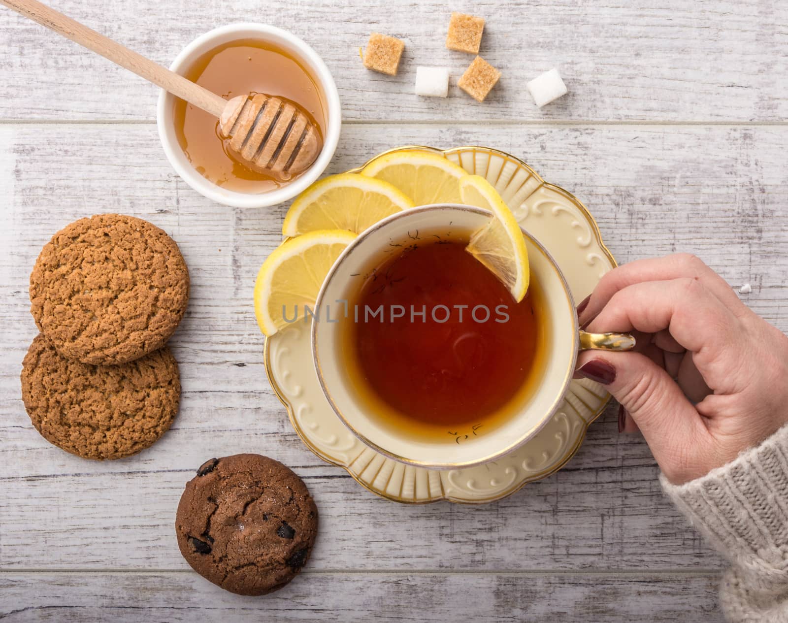 woman drinking tea with lemon . cookies, sugar , honey  lying on a white wooden table. 