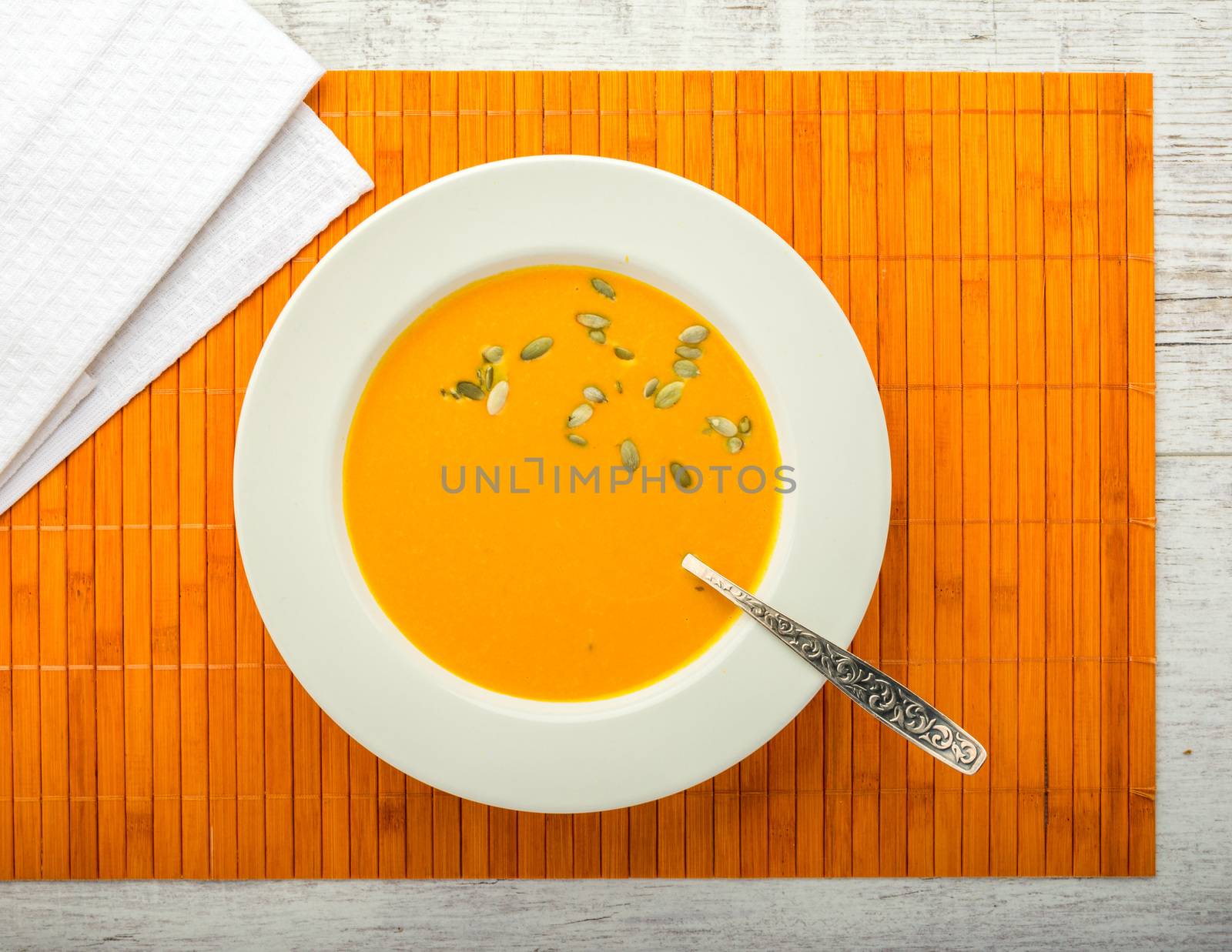 pumpkin cream soup with pumpkin seeds in a white plate with a spoon on a orange napkin closeup