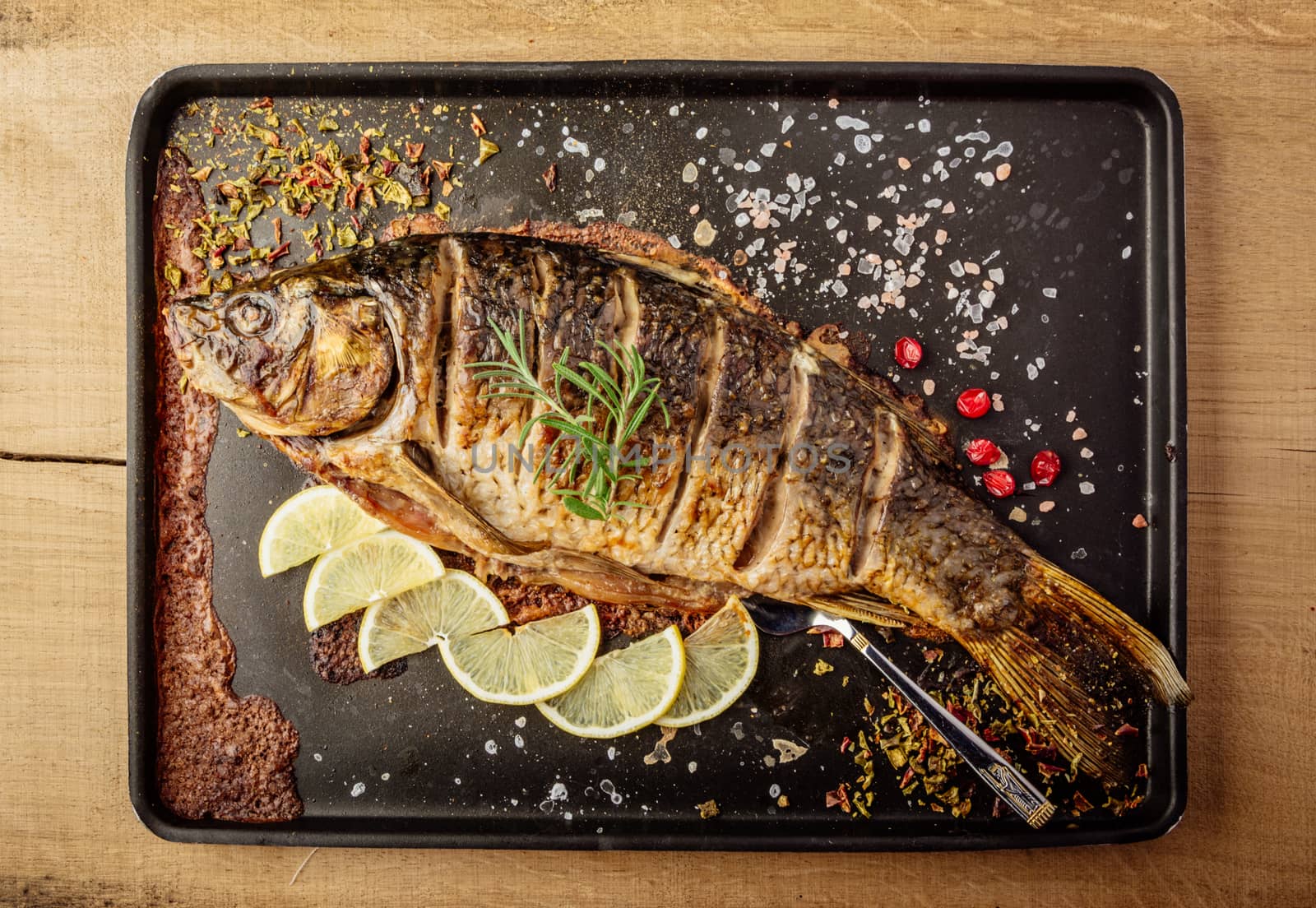 baked carp with spices and lemon on black pan