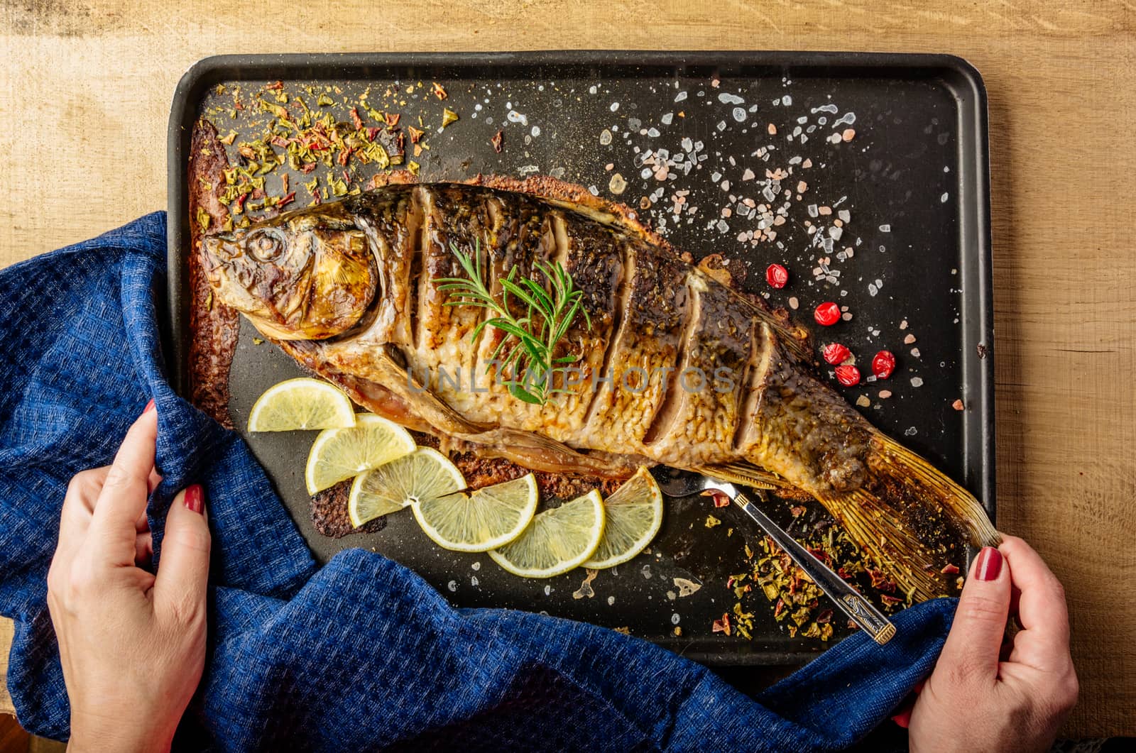 chef holds baked carp with spices and lemon on black pan