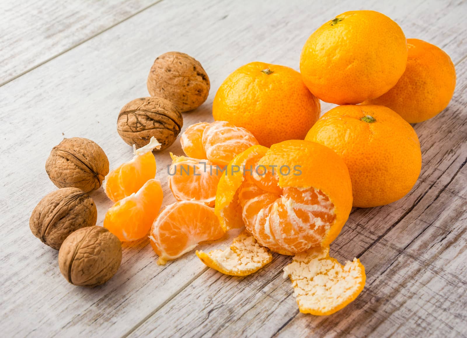 tangerines, peeled tangerine, tangerine slices and walnuts on a white wooden table