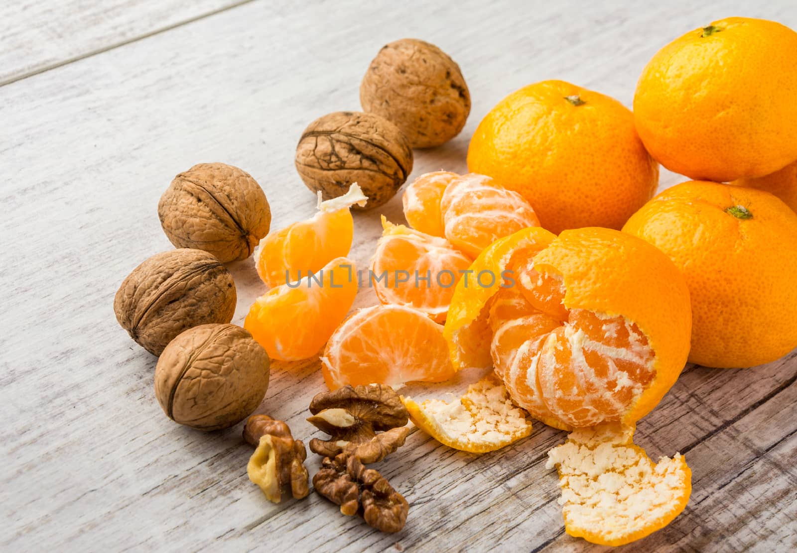 tangerines, peeled tangerine, tangerine slices and walnuts on a white wooden table