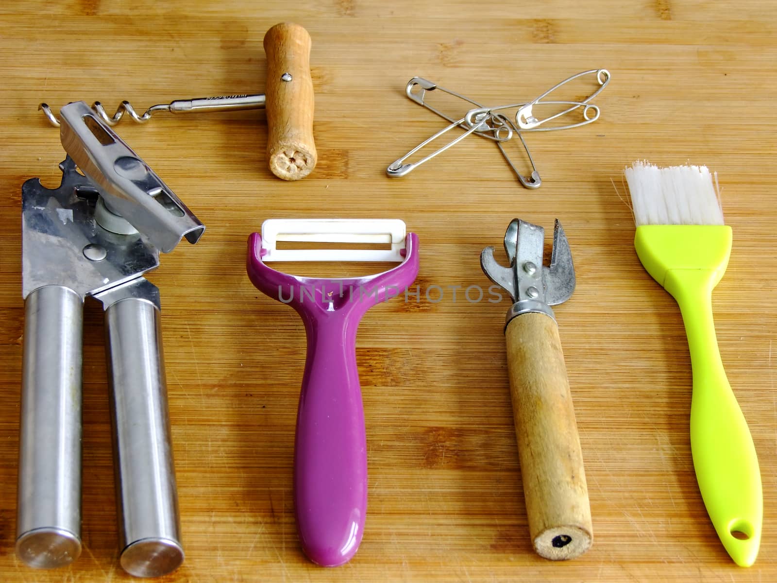 Two different Can Openers, Brush, Potato Peeler, Bottle Opener and Safety Pins on wooden Cutting Board