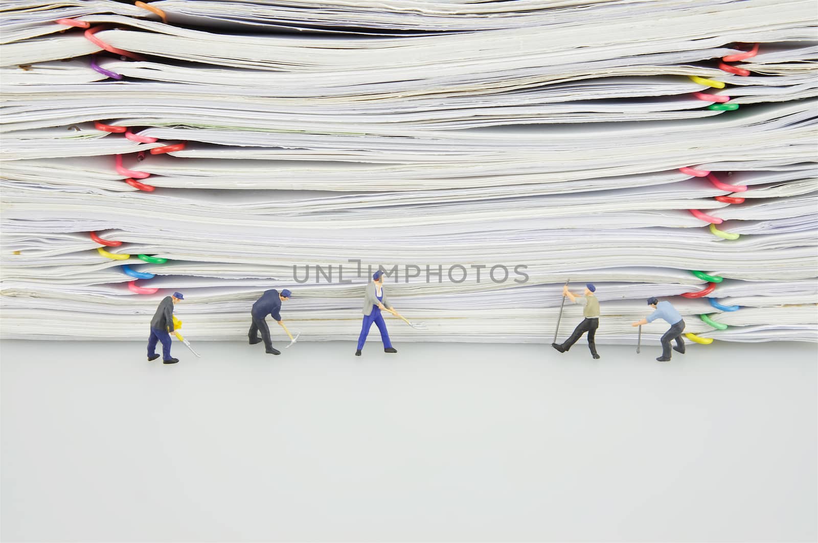 Pile overload paper with colorful paperclip and miniature people are destroyed it on white background.