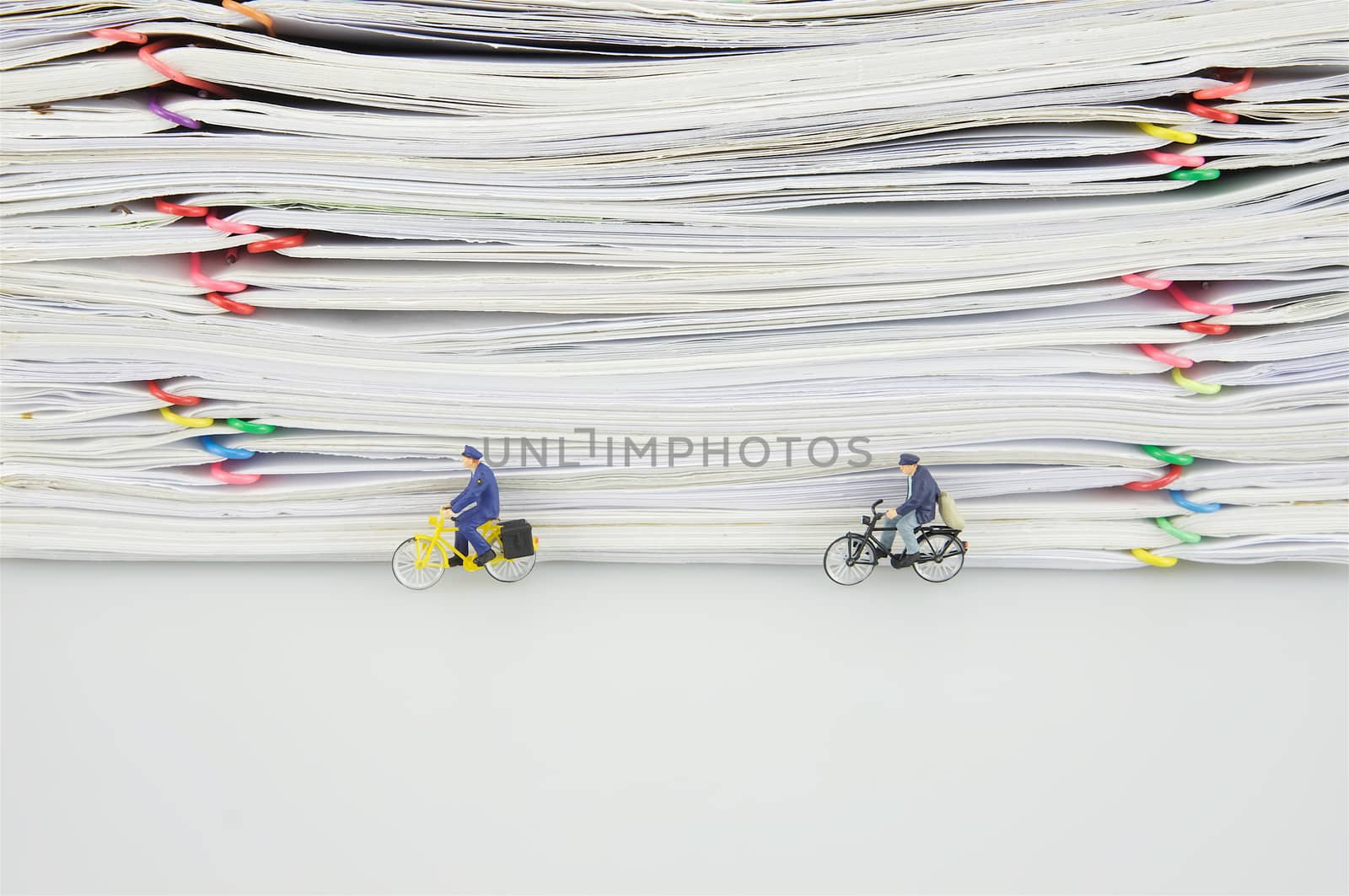 Pile overload paper with colorful paperclip and miniature people are bicycling on white background.
