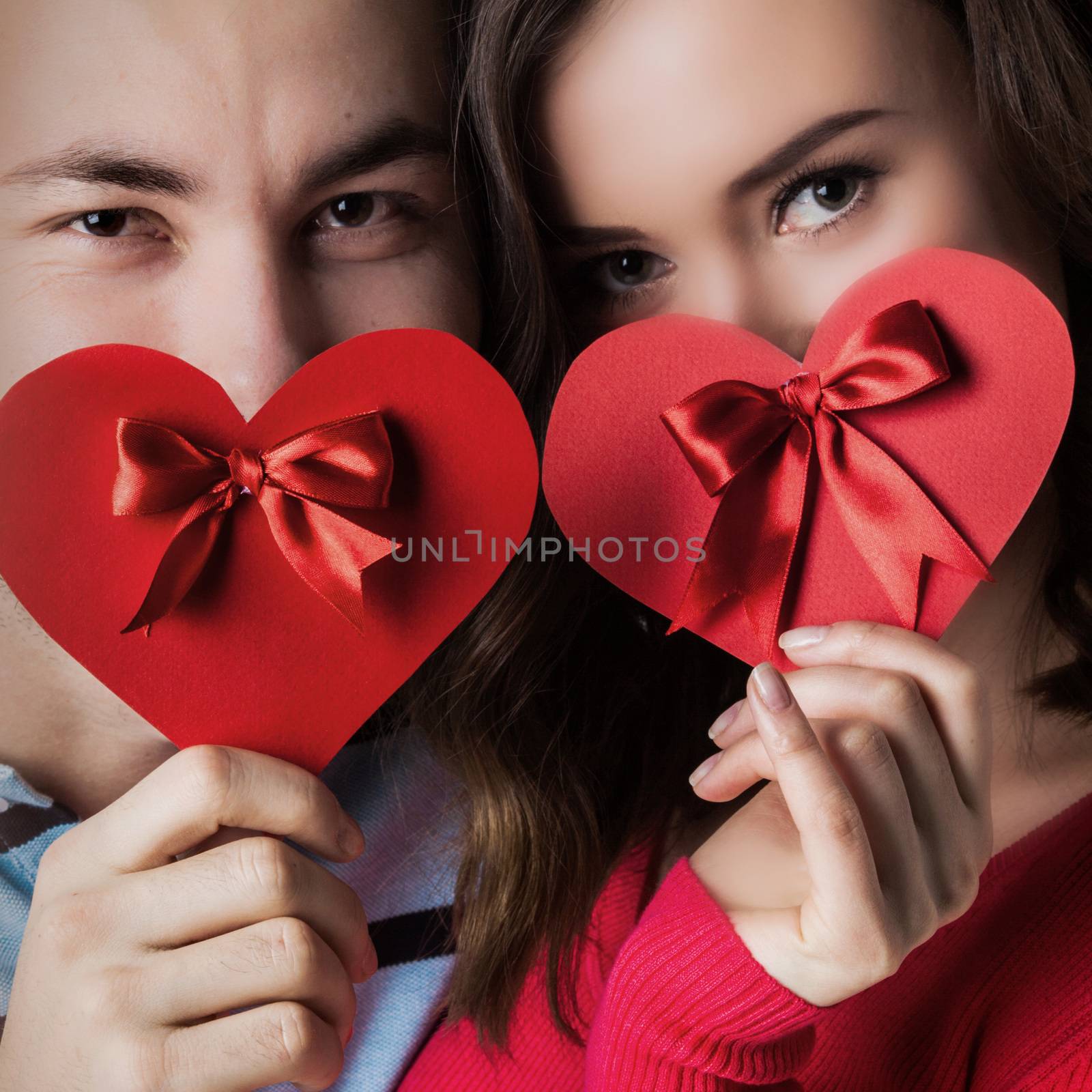 Young couple holding valentine's greeting red heart cards with bows, valentine day concept