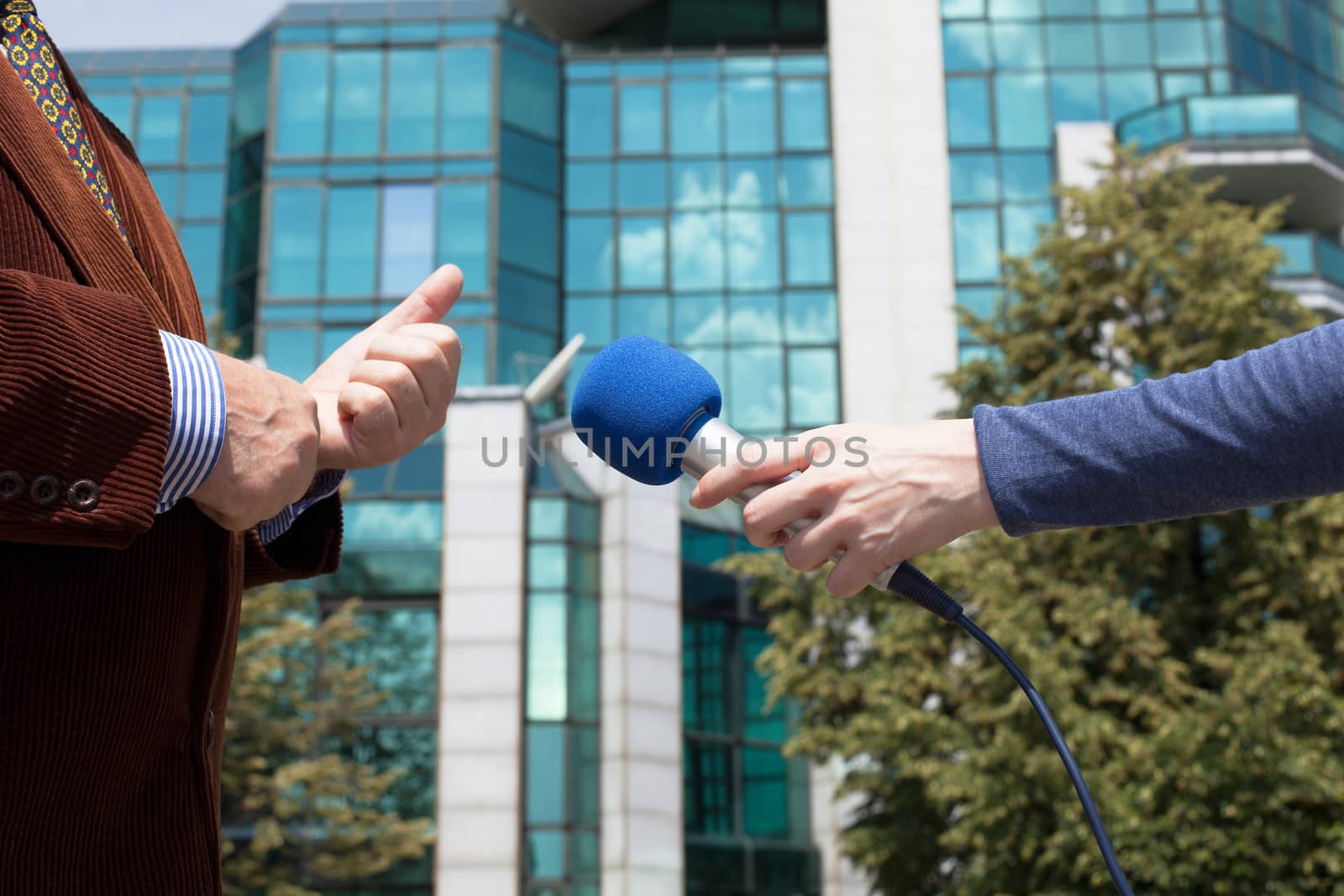 Reporter interviewing businessman, corporate building in background by wellphoto