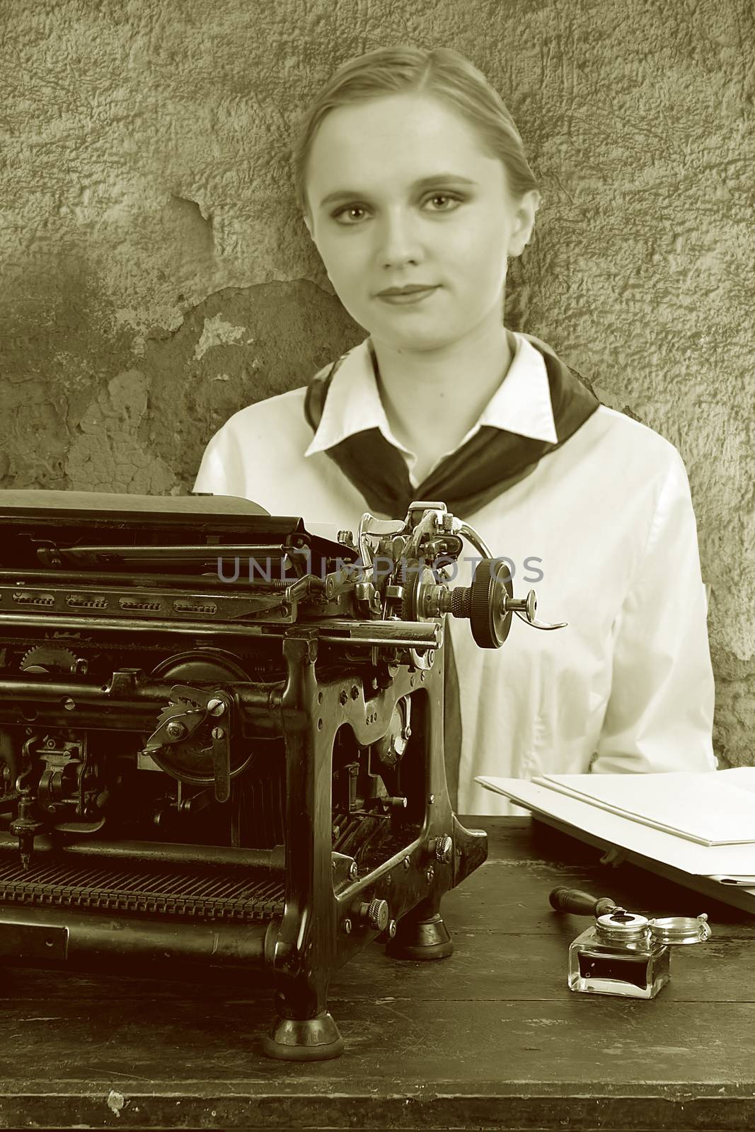 Nice girl for a vintage typewriter in retro style on background of old wall