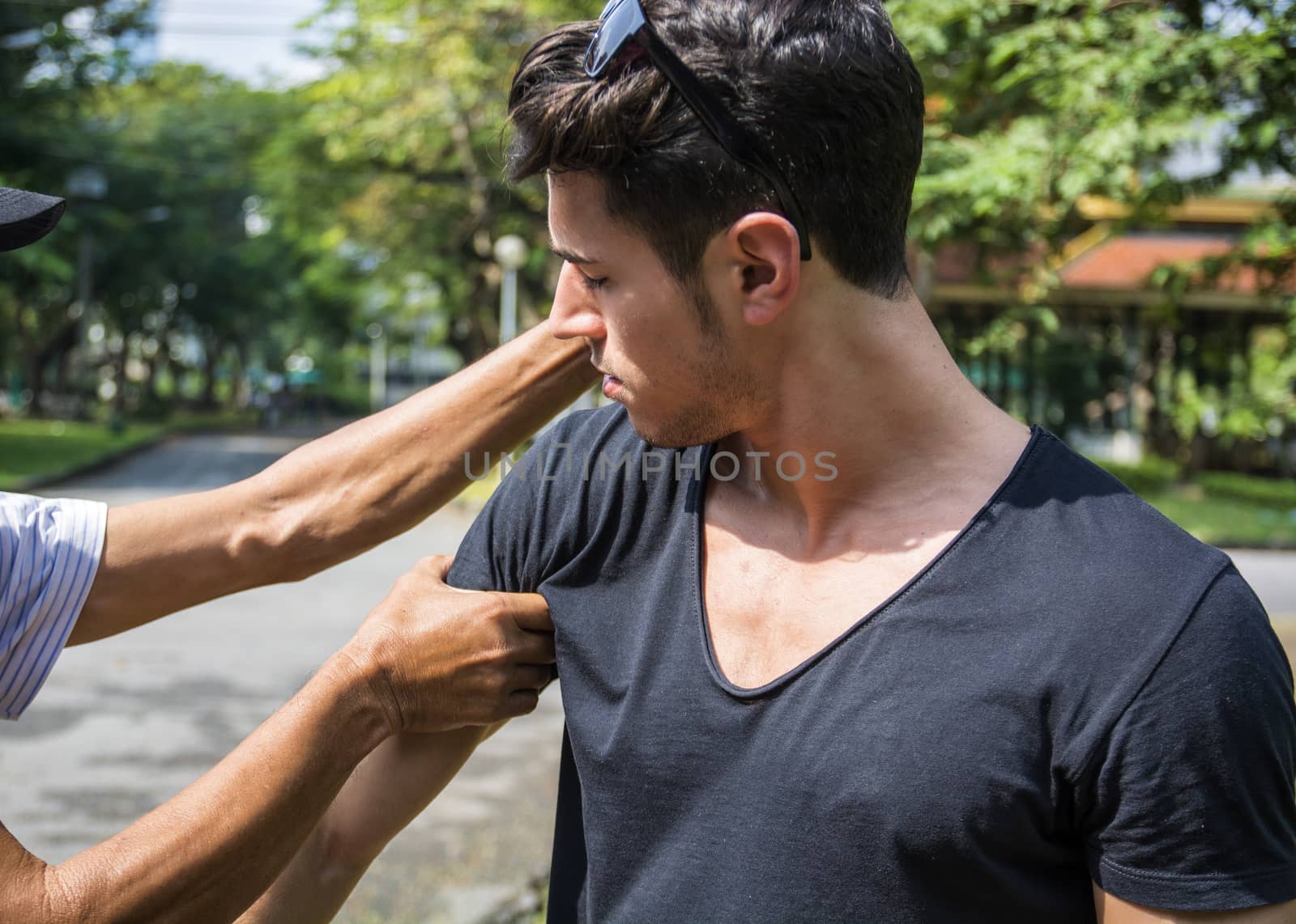 Young man standing and receiving hand massage. Horizontal outdoors shot