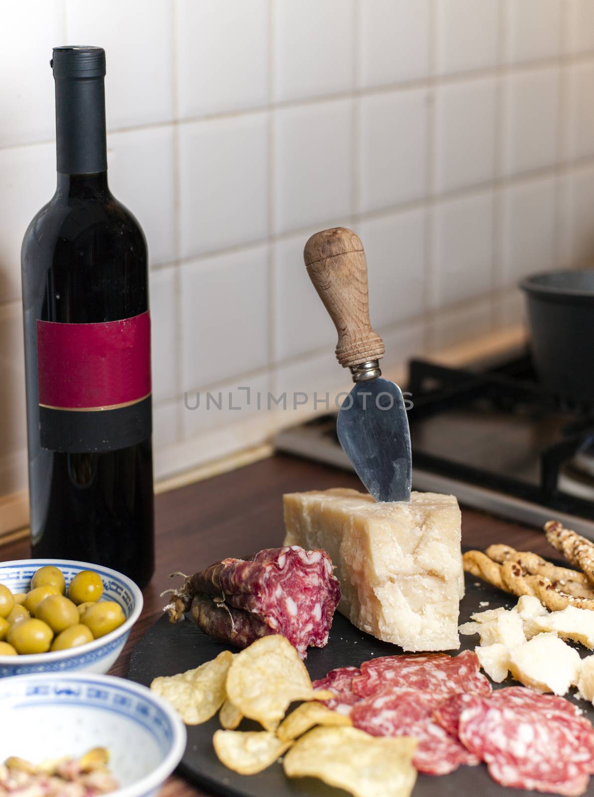 A dark stone tray on a wooden kitchen table filled with parmesan cheese, salami and potato chips.