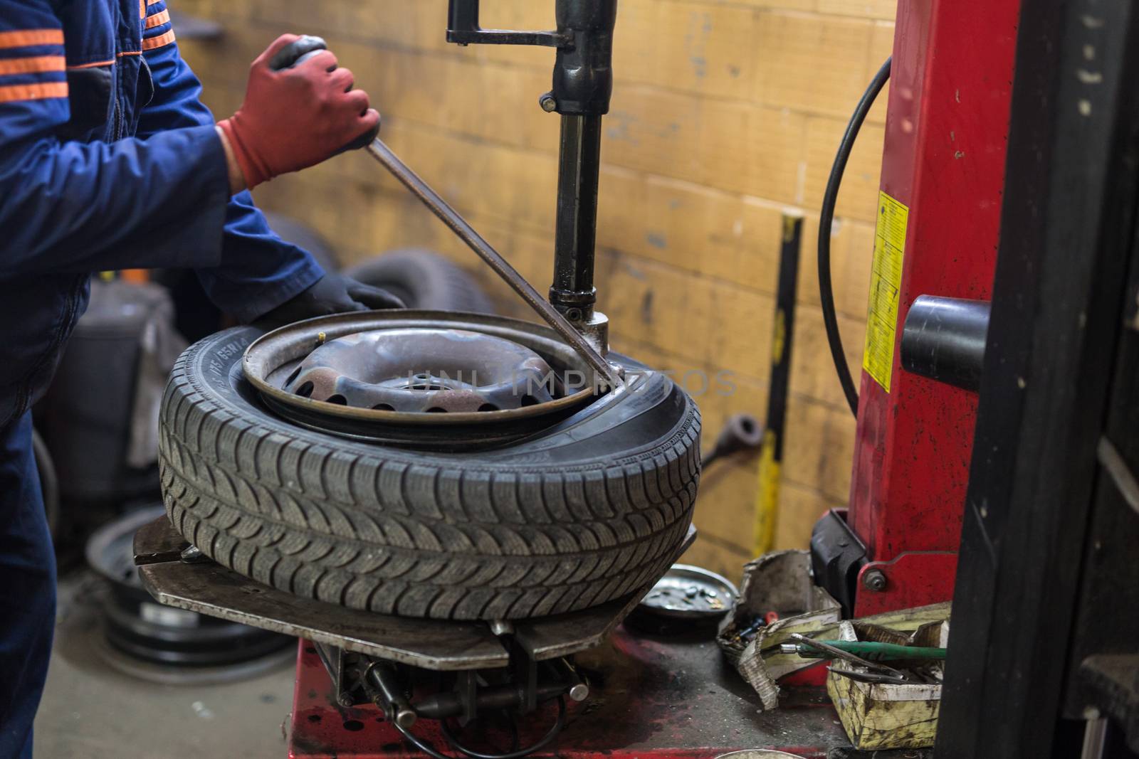 Professional auto mechanic replacing tire on wheel in car repair workshop.