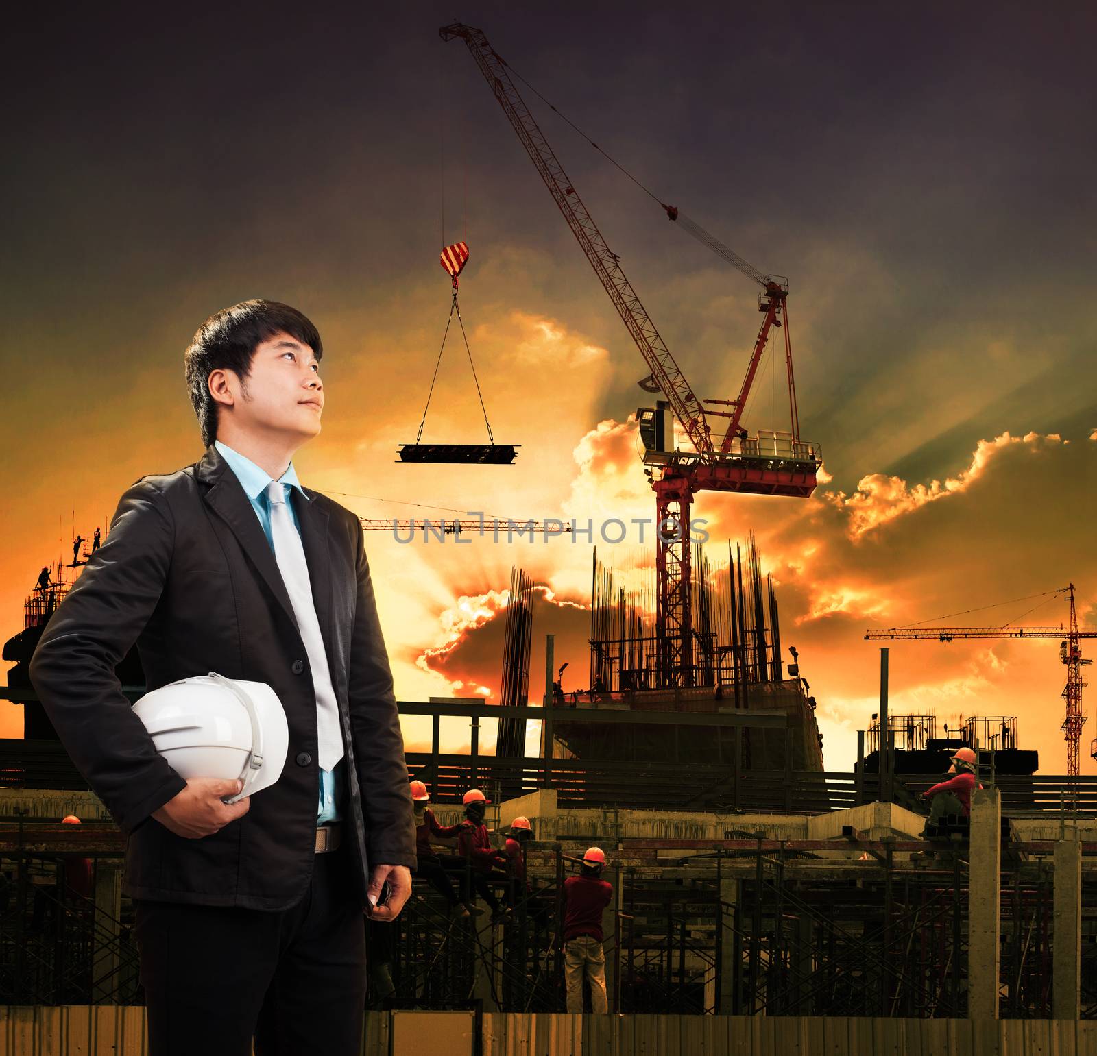 engineering man and safety helmet standing against crane constru by khunaspix