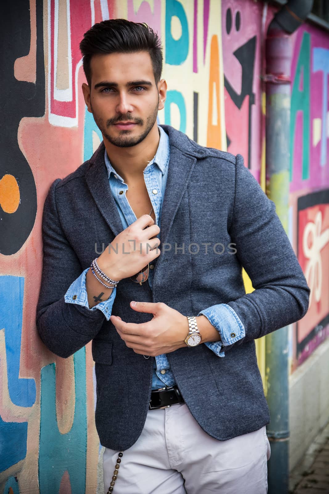 Attractive young man standing against colorful graffiti wall, looking at camera