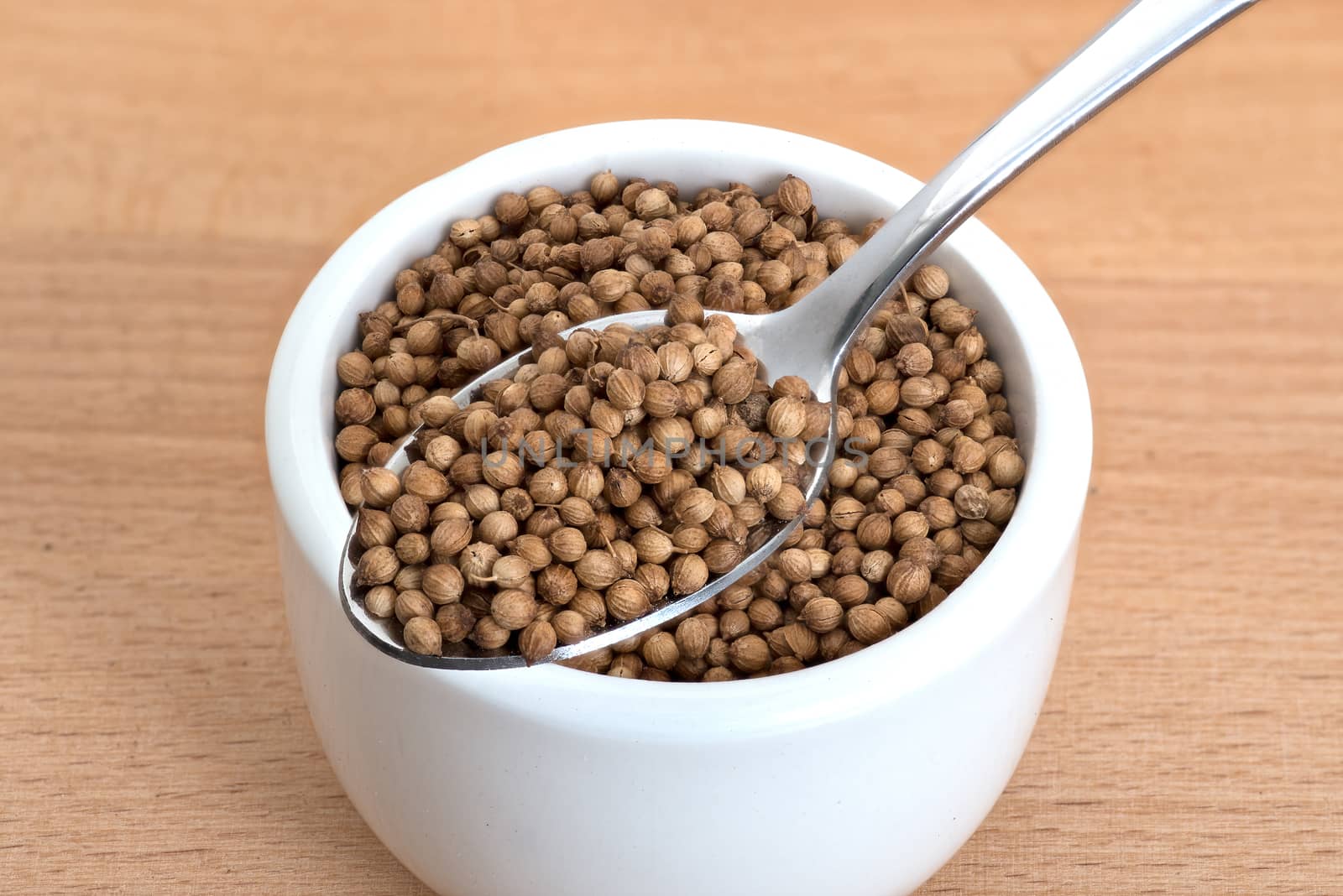 Organic coriander seeds spoon and in small white bowl on wooden cutting board