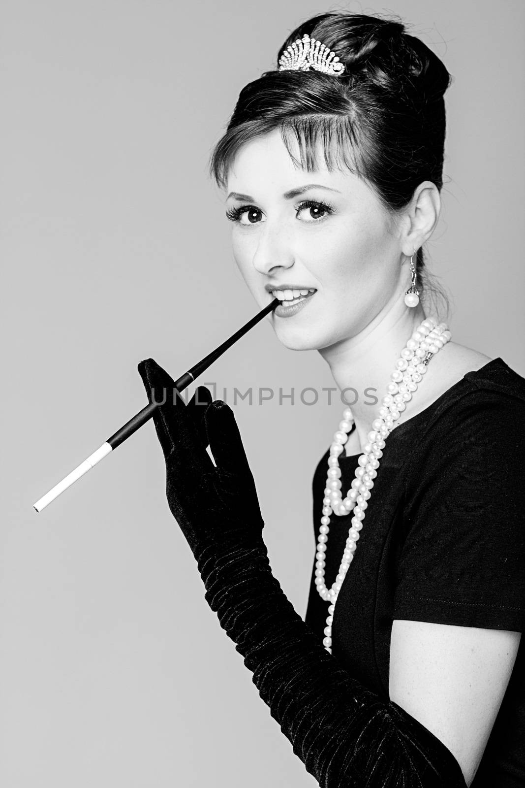 Portrait of a beautiful young woman in retro style with cigarette in mouthpiece in the image of the famous actress Audrey Hepburn. Black and white photography