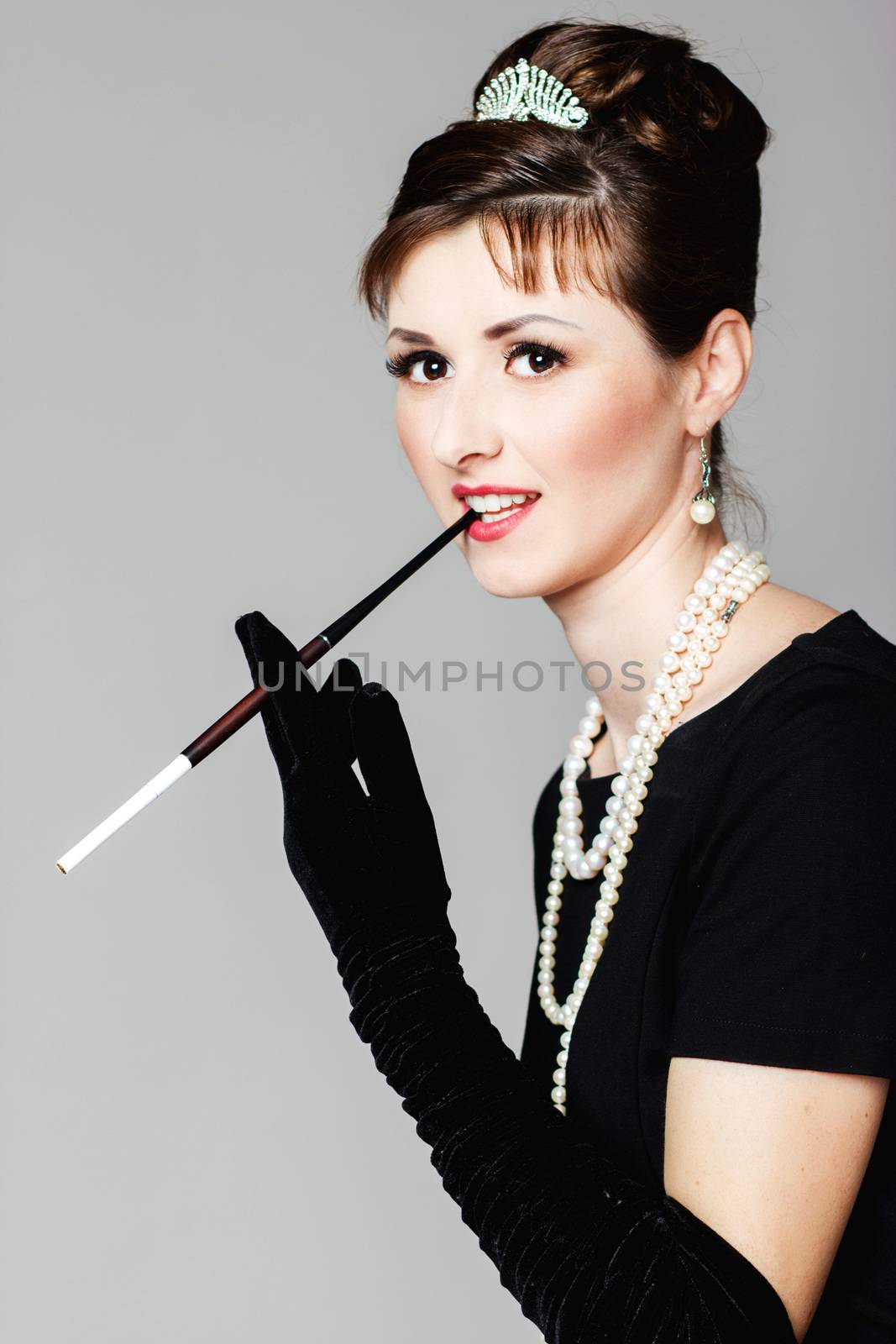 Portrait of a beautiful young woman in retro style with cigarette in mouthpiece in the image of the famous actress Audrey Hepburn
