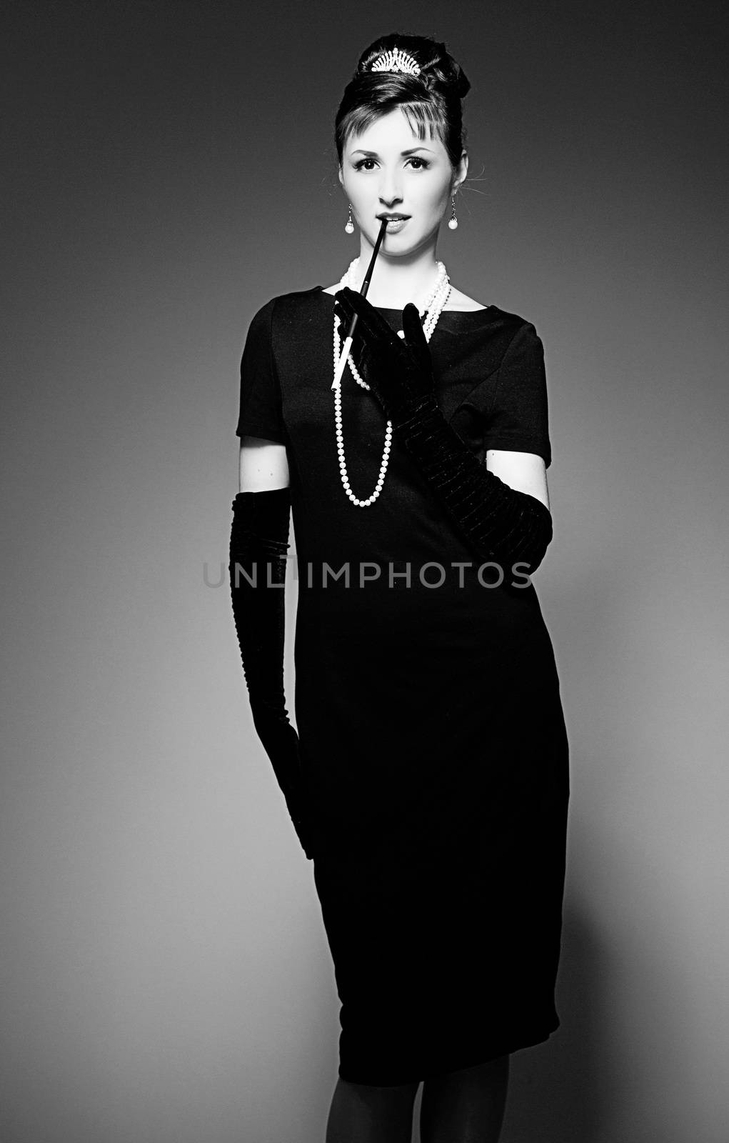 Portrait of a beautiful young woman in retro style with cigarette in mouthpiece in the image of the famous actress Audrey Hepburn. Black and white photography