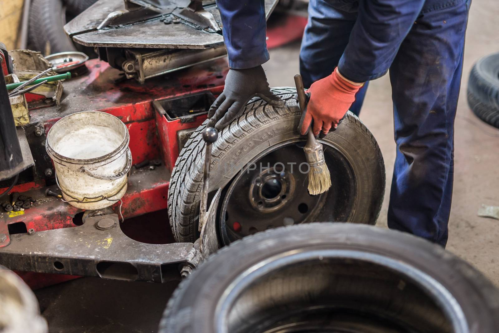Professional auto mechanic replacing tire on wheel in car repair workshop.
