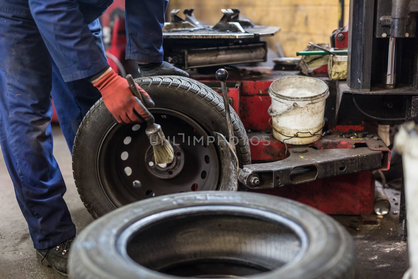 Professional auto mechanic replacing tire on wheel in car repair workshop.